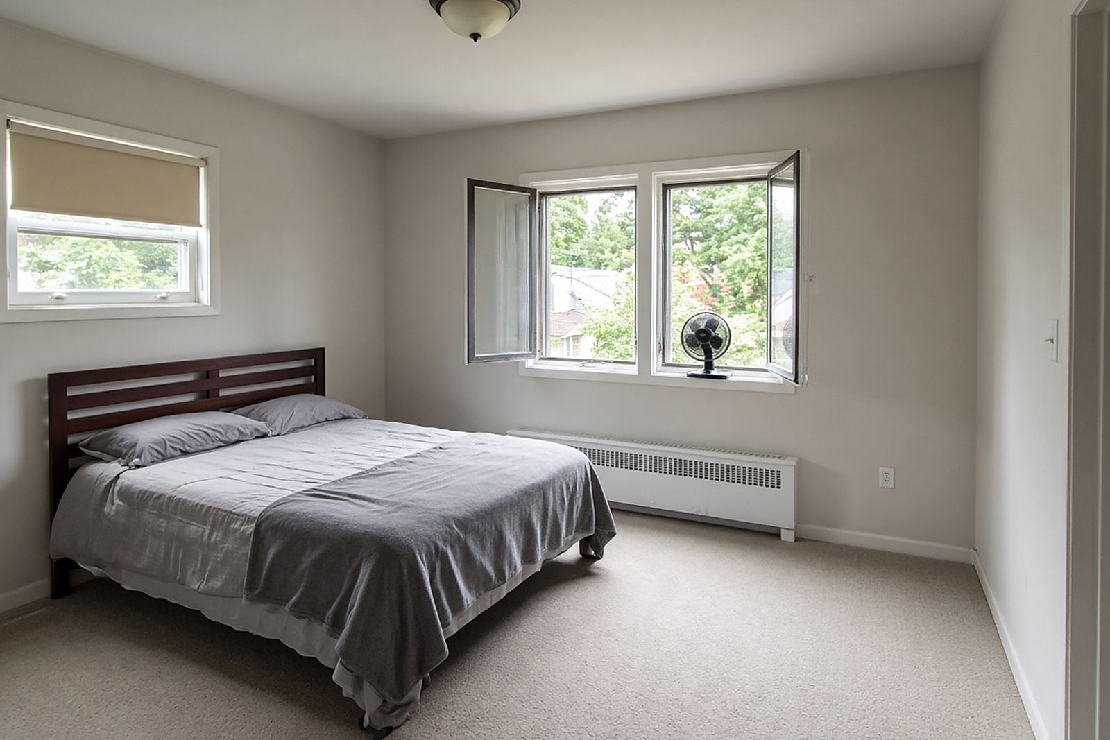 Bright bedroom with a made bed, open windows and a small fan running